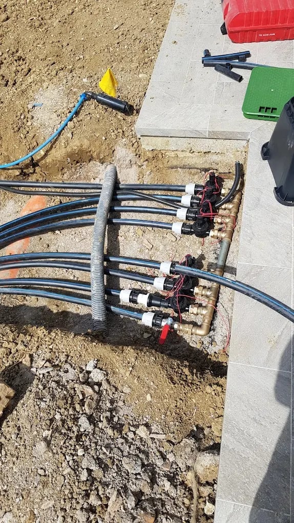 Construction site electrical junction box with multiple blue cables and connections embedded in concrete, surrounded by dirt and tools