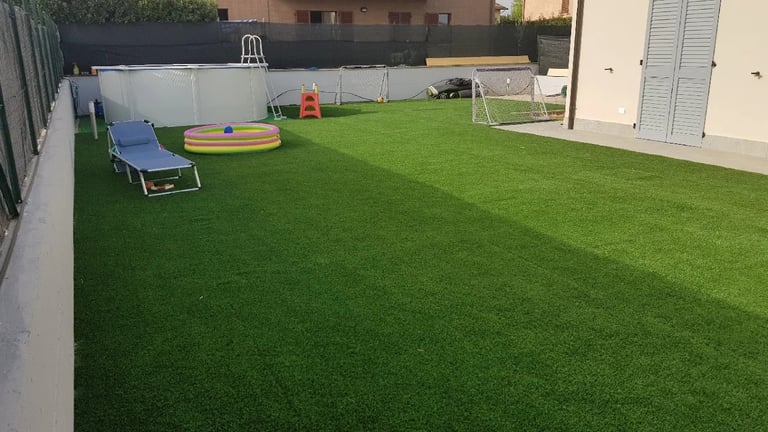 Spacious backyard with artificial green turf, blue lounger chair, colorful play ring, and soccer goal against fence
