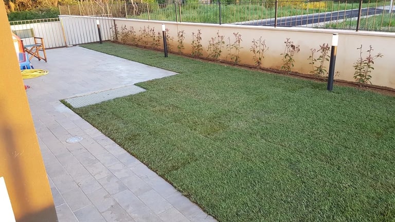 Backyard patio with artificial green turf, concrete pavers, metal fencing, and a yellow column structure